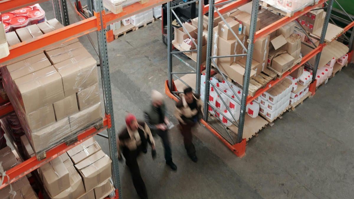 A high angle view of workers in motion in a busy warehouse with shelves full of boxes and packages.