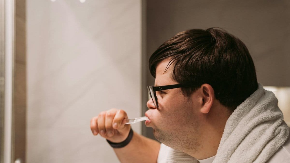 Side view of a man brushing teeth in bathroom, promoting daily dental care and hygiene.