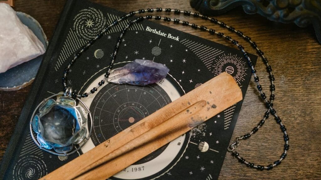 Astrology-themed flat lay featuring a birthdate book, crystals, and necklace on a wooden surface.