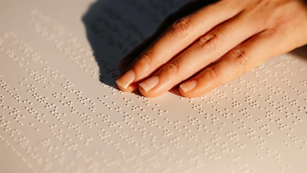 Hand feeling Braille text on paper, highlighting tactile reading for the visually impaired.