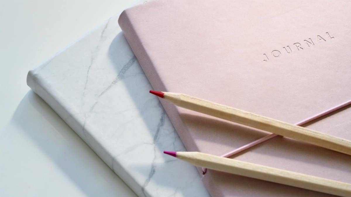 Close-up of a pink journal with pencils on a marble top. Perfect for note-taking or planning.