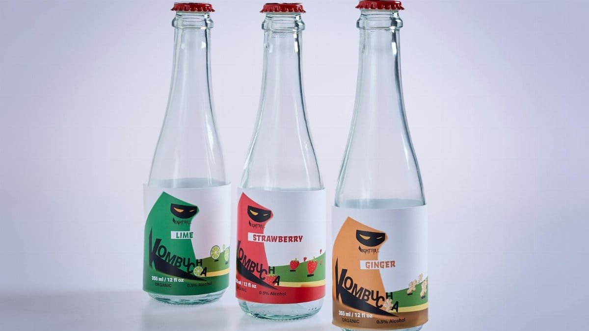 Three labeled kombucha bottles featuring lime, strawberry, and ginger flavors on a white surface.