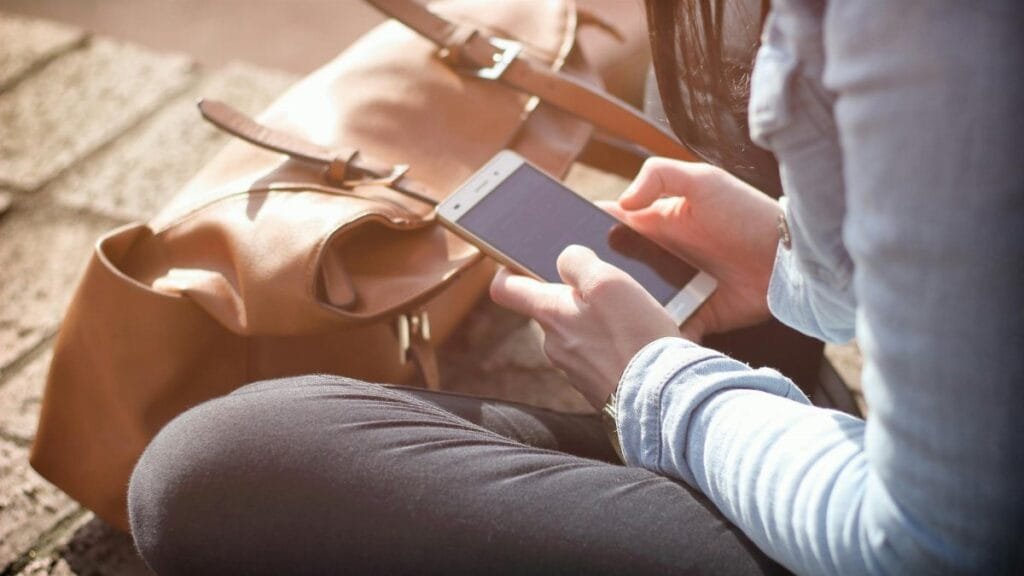 Woman sitting with smartphone and brown bag in sunlight.