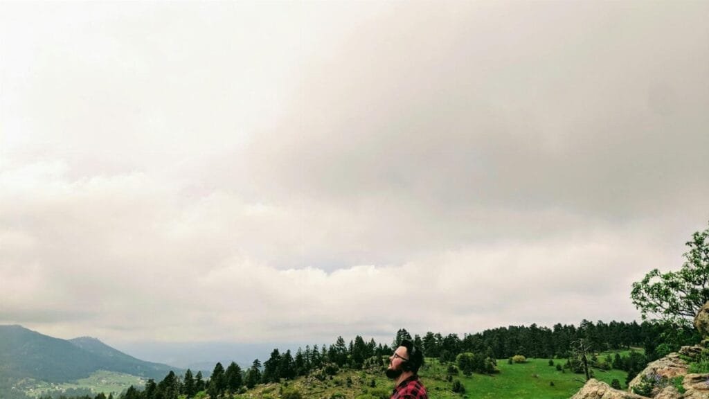 A man in a checkered shirt enjoys a quiet moment in the scenic mountains of Indian Hills, Colorado.