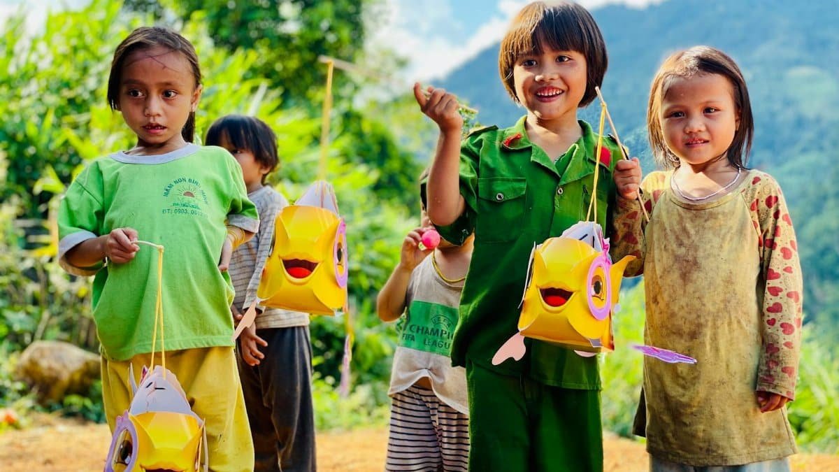 Happy children holding fish-shaped lanterns in scenic Nam Trà My, Vietnam.