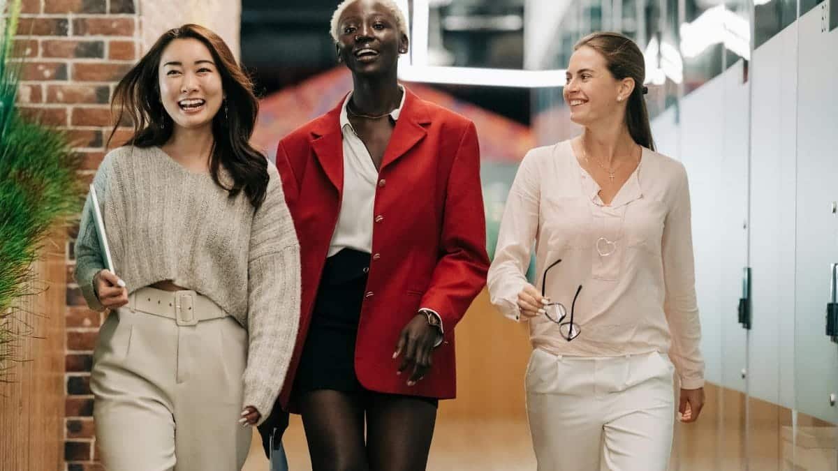 Three diverse and confident businesswomen walking together in a modern office hallway, exuding professionalism and joy.