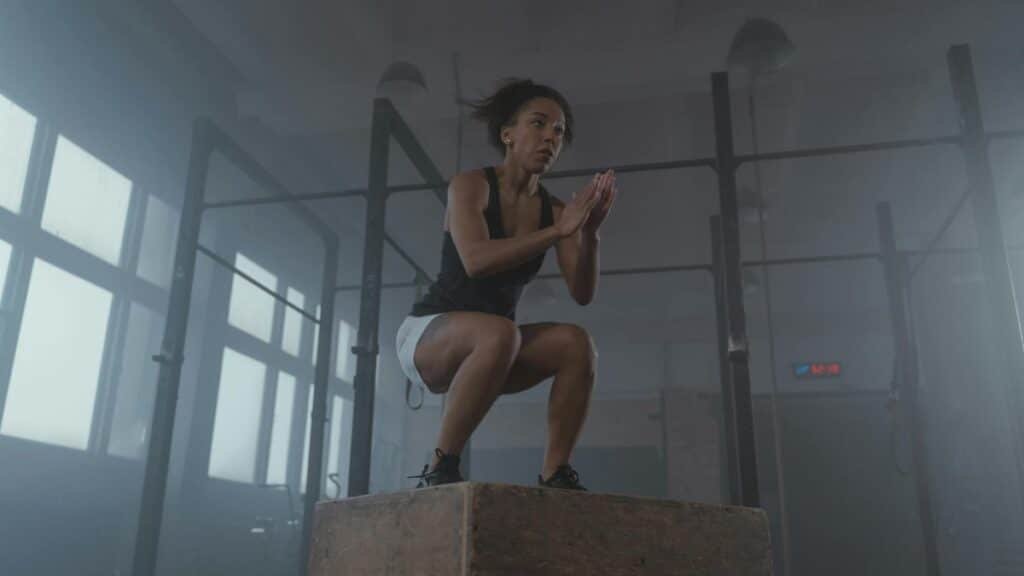 A determined woman executing a box jump in an indoor gym setting, showcasing strength and fitness.