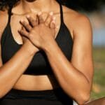 A woman in activewear practices mindfulness meditation outdoors, hands on chest.