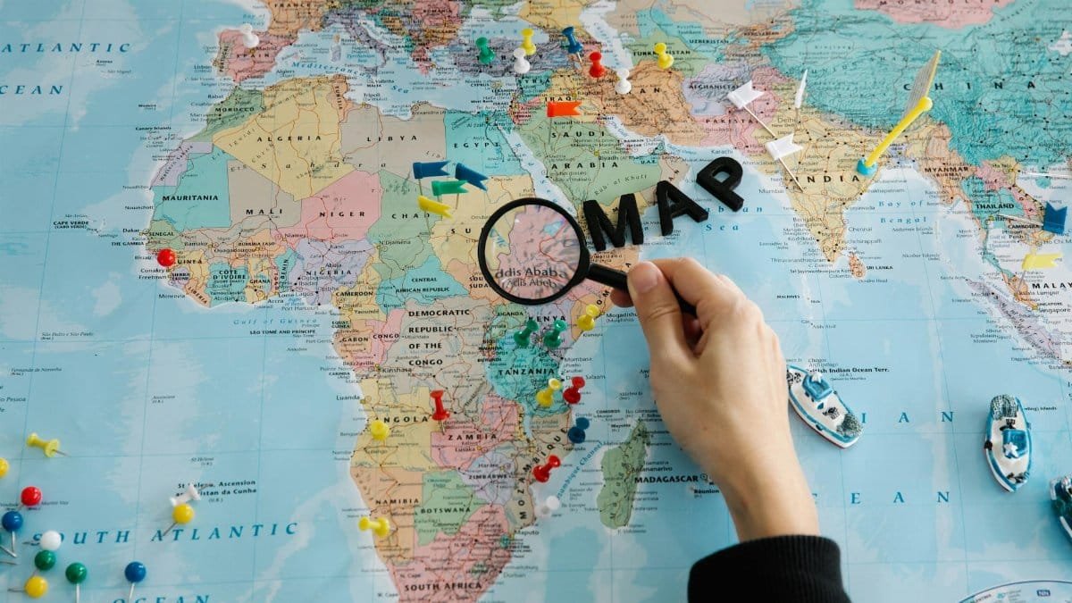 Hand using magnifying glass on a colorful map, with pins and miniature boats.