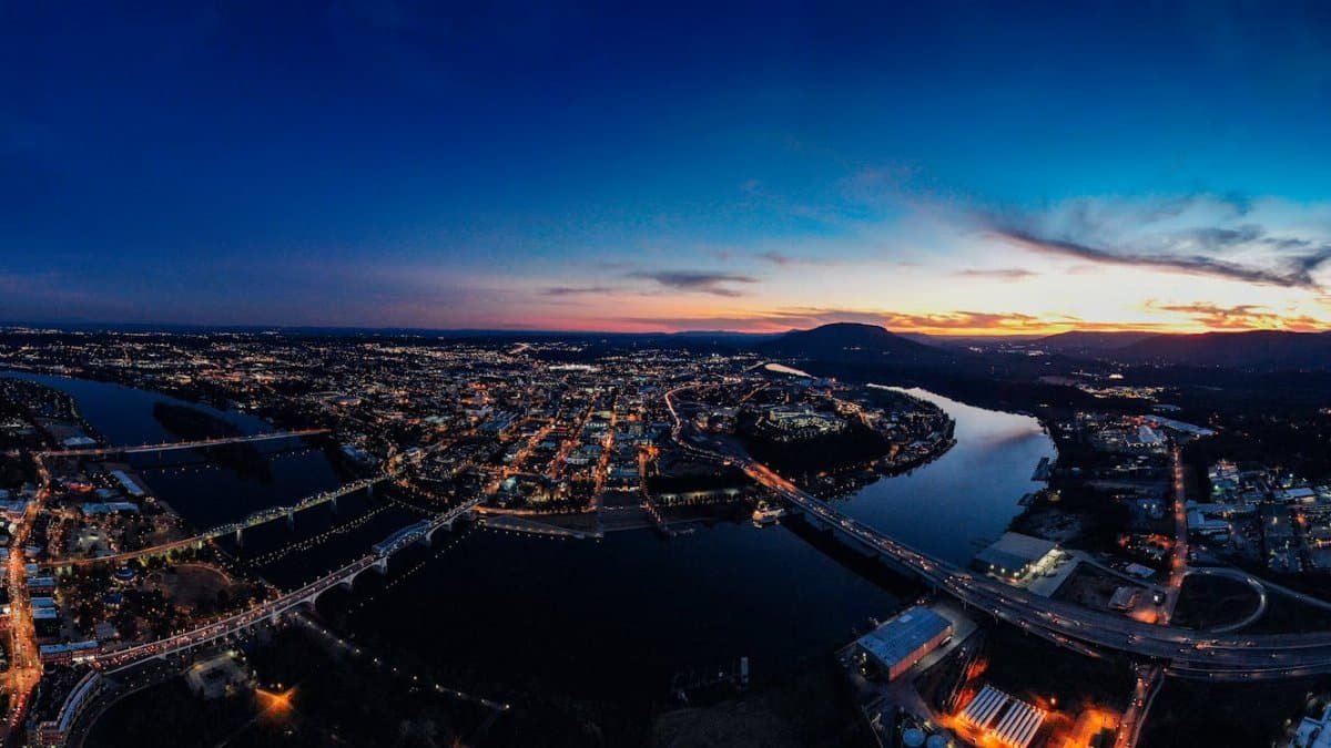 A breathtaking aerial view of a cityscape bathed in twilight with vibrant city lights reflecting on a winding river.