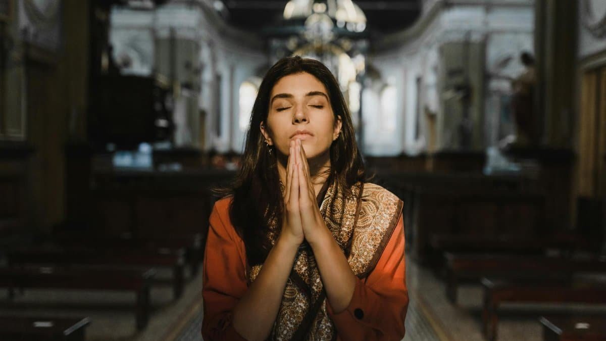 A woman with closed eyes prays in a peaceful cathedral setting, conveying a sense of calm and spirituality.