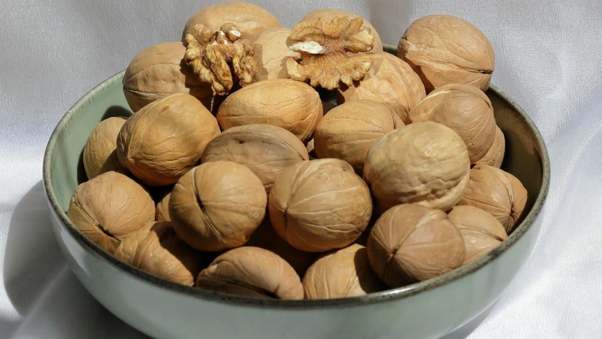 A bowl of whole and cracked walnuts on white fabric, highlighting texture and natural color.