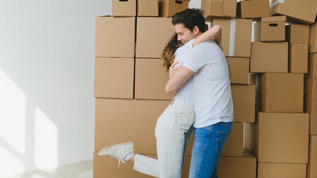 A cheerful couple hugs surrounded by moving boxes, celebrating their new home.