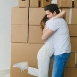 A cheerful couple hugs surrounded by moving boxes, celebrating their new home.