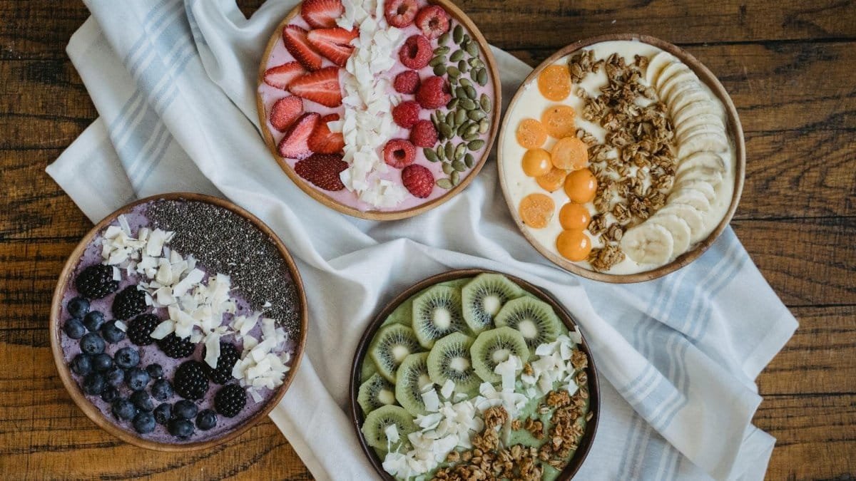 Top view of colorful smoothie bowls with a variety of fresh fruits and toppings on a wooden table.