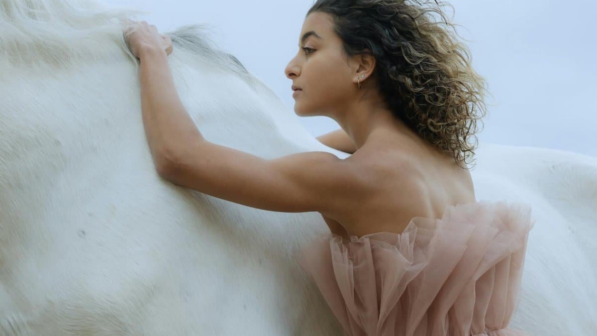 A woman with curly hair in a dress embraces a white horse, showcasing grace and elegance.