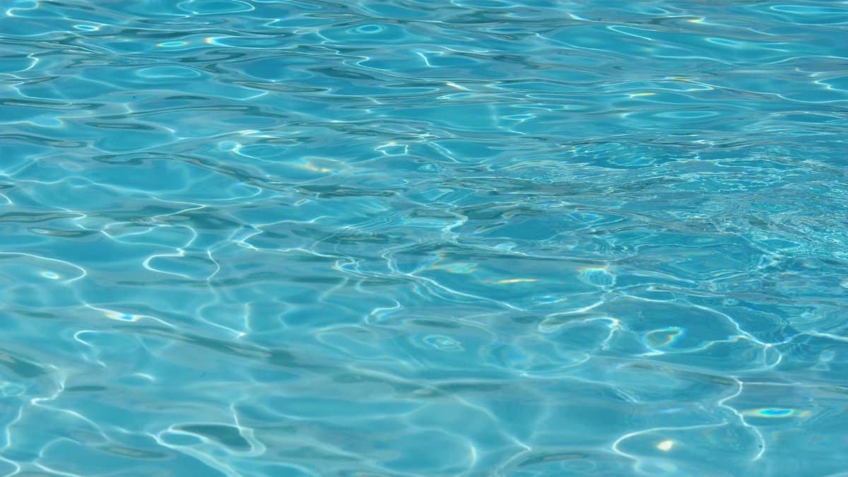 A vibrant turquoise water surface, showcasing clear ripples and captivating patterns. Perfect for summer themes.