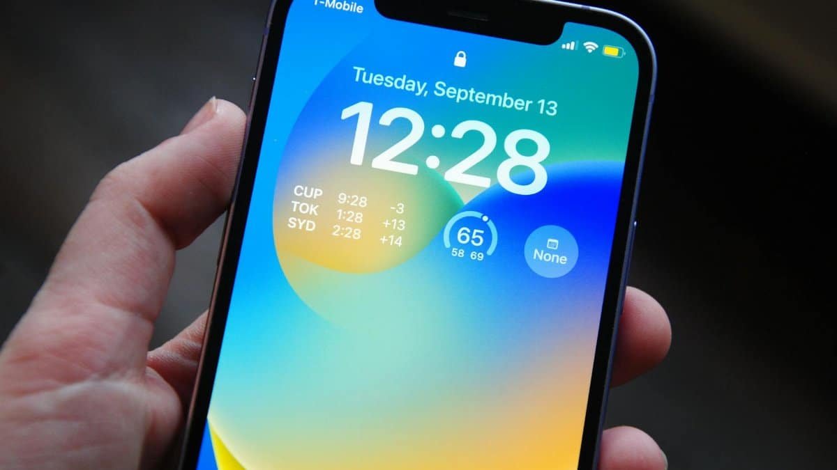 Close-up of a hand holding a smartphone showing a vibrant lock screen with time and date details.