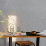 A minimalist scene of a table with flowers, an open book, and wooden bowl, enhanced by natural lighting.