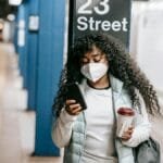 African American woman using phone at 23 Street subway, NYC. COVID-19 precautions.