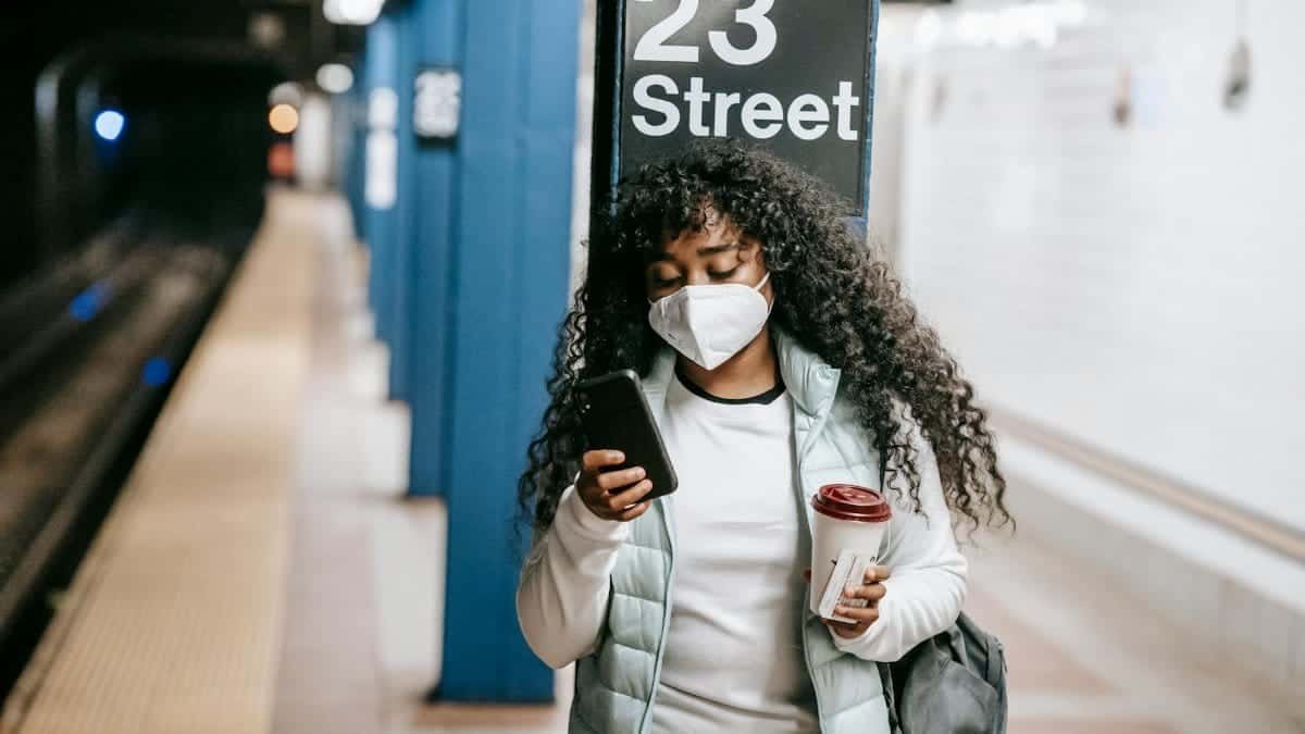 African American woman using phone at 23 Street subway, NYC. COVID-19 precautions.