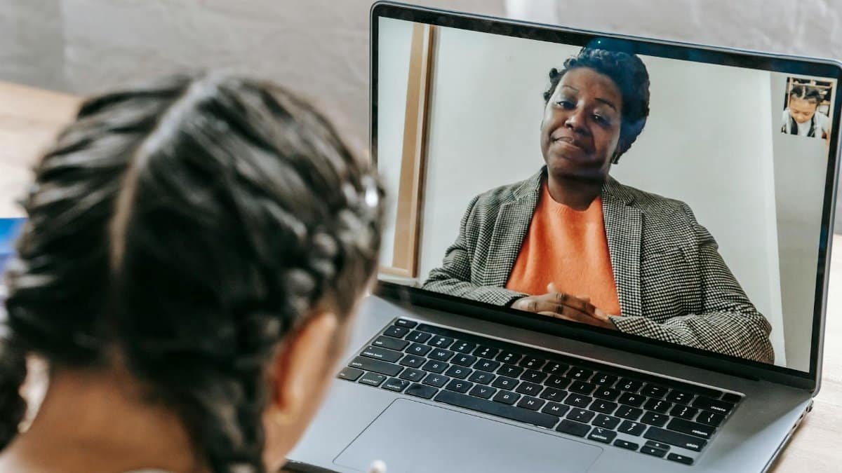 Child using laptop for online learning with teacher on video call, enhancing education at home.