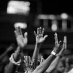 A group of people raising hands in a black and white concert setting, showing unity and celebration.