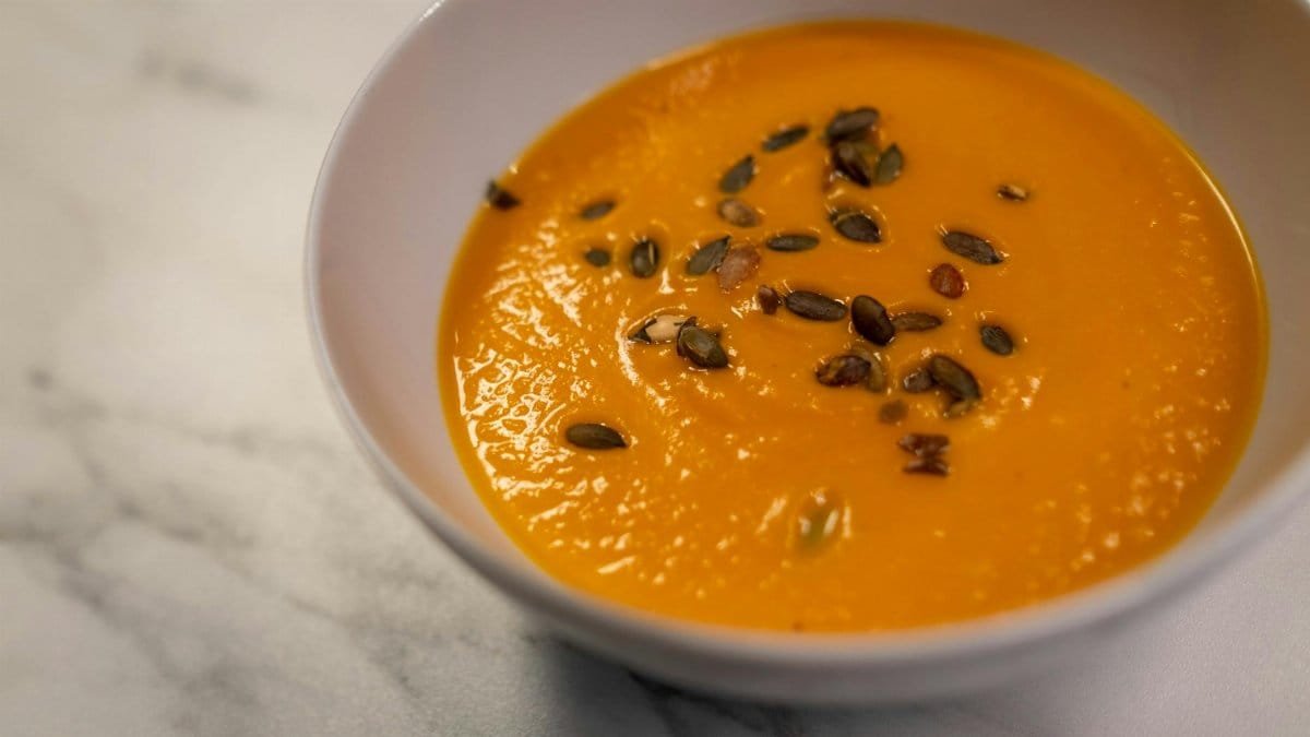 Close-up of a creamy pumpkin soup garnished with roasted seeds in a bowl.