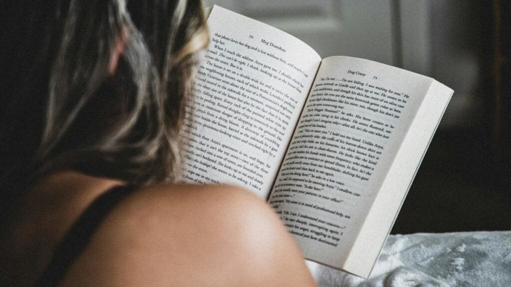 A woman reads a novel in bed, enjoying a quiet moment indoors, showcasing relaxation and literature.