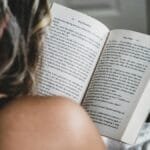A woman reads a novel in bed, enjoying a quiet moment indoors, showcasing relaxation and literature.