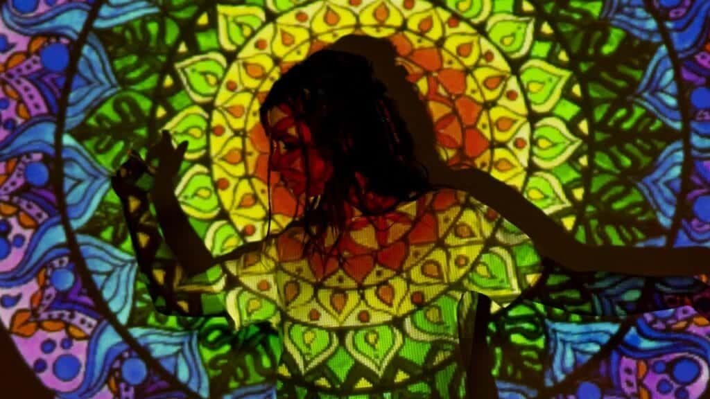 A vibrant mandala pattern projected onto a woman's silhouette, creating an artistic, esoteric atmosphere.