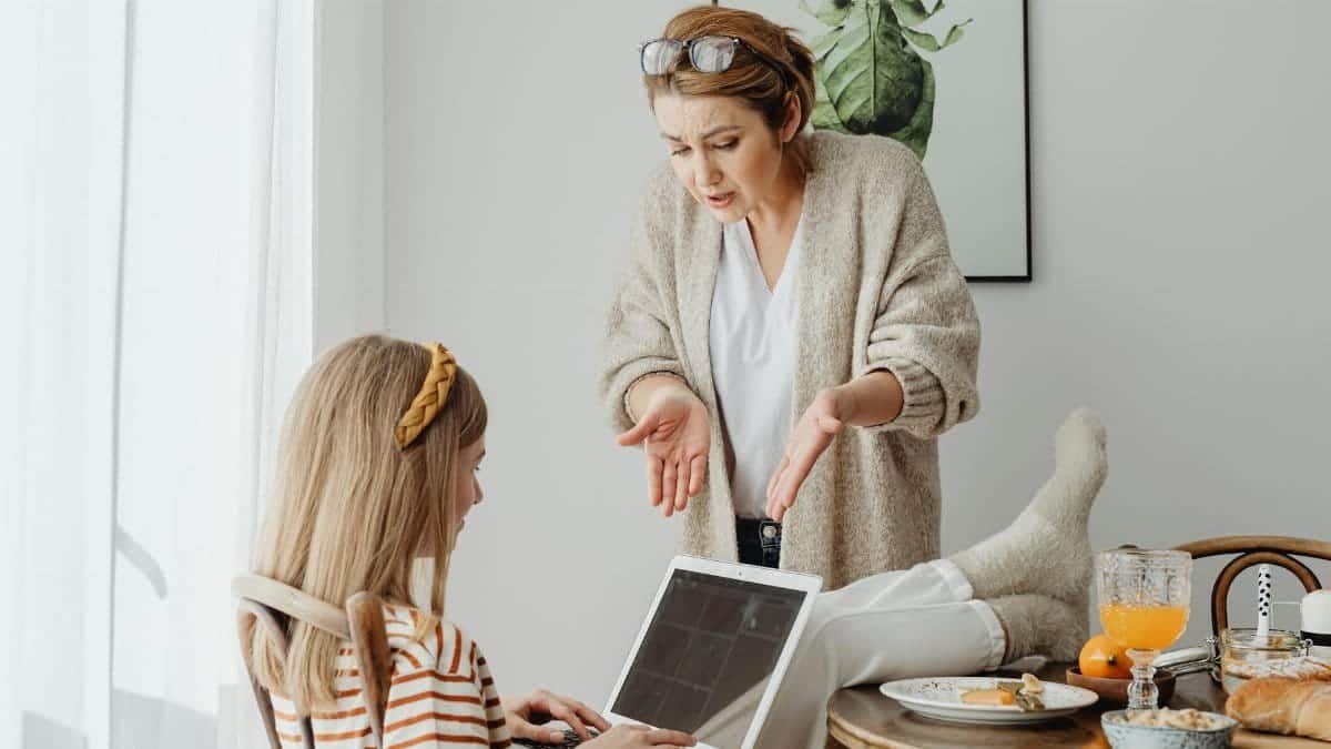 A mother scolds her teenage daughter absorbed in her laptop during breakfast at home.