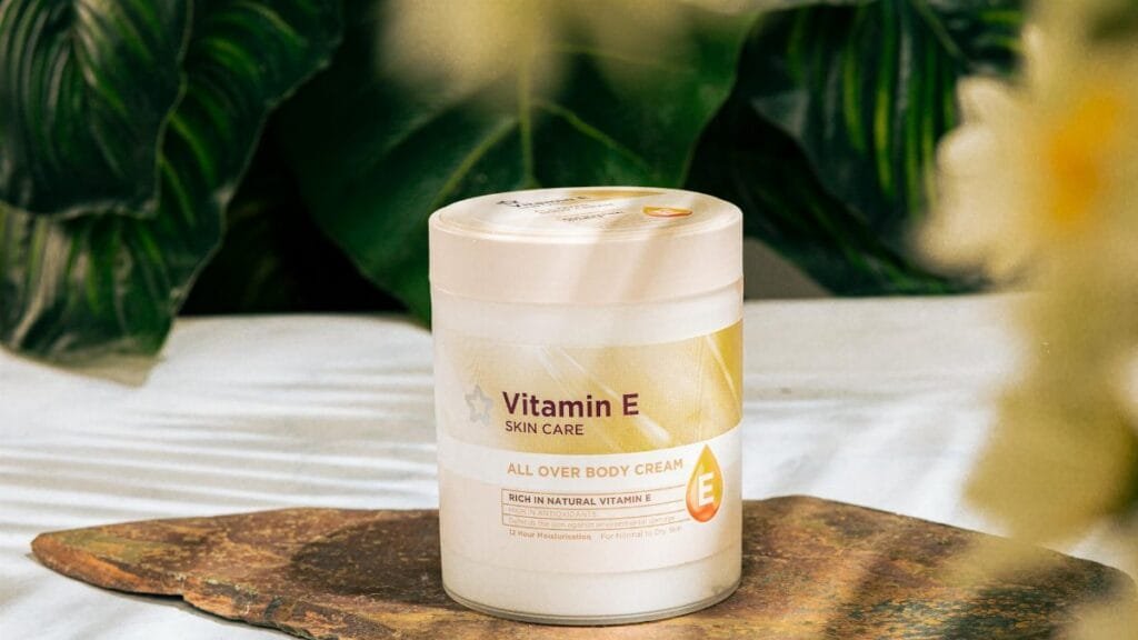 Vitamin E skin care cream jar displayed on a natural stone surface surrounded by lush green leaves.