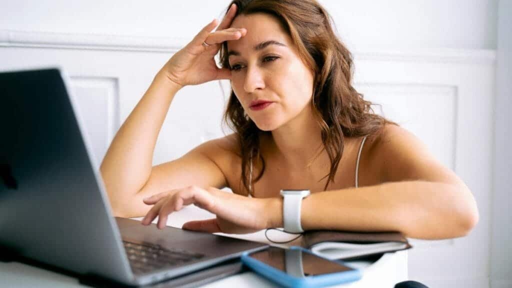 A woman with a frustrated expression, hand on head, working on a laptop.
