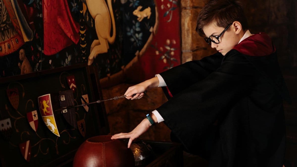 A child dressed as a wizard holding a wand and engaging in fantasy play indoors.