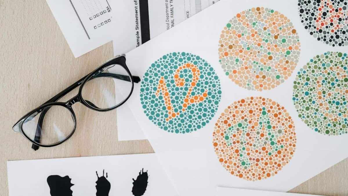 Close-up of color blindness test sheets with eyeglasses on a wooden table.