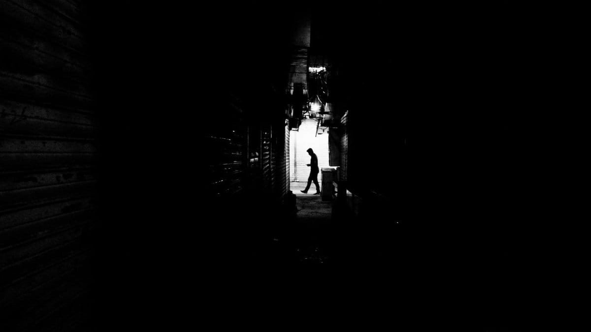 Black and white photo capturing a silhouette of a man walking in a dimly lit alley.