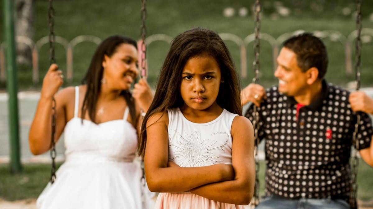 A young girl looking grumpy while her parents enjoy swings in a park.