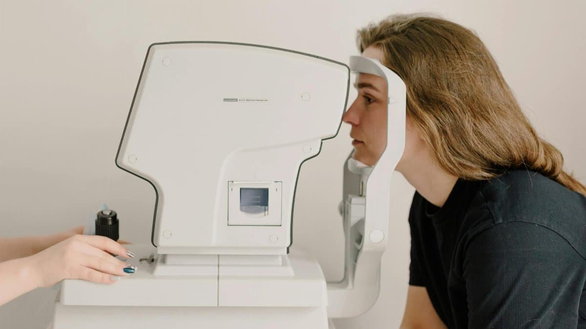 Side view of crop anonymous doctor checking eyesight of female patient using vision screening device in clinic