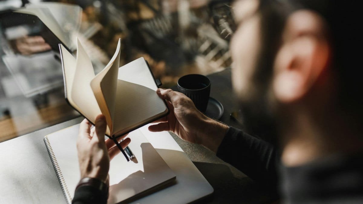 A person flips through a notebook while seated by a window, enjoying a cozy ambiance.
