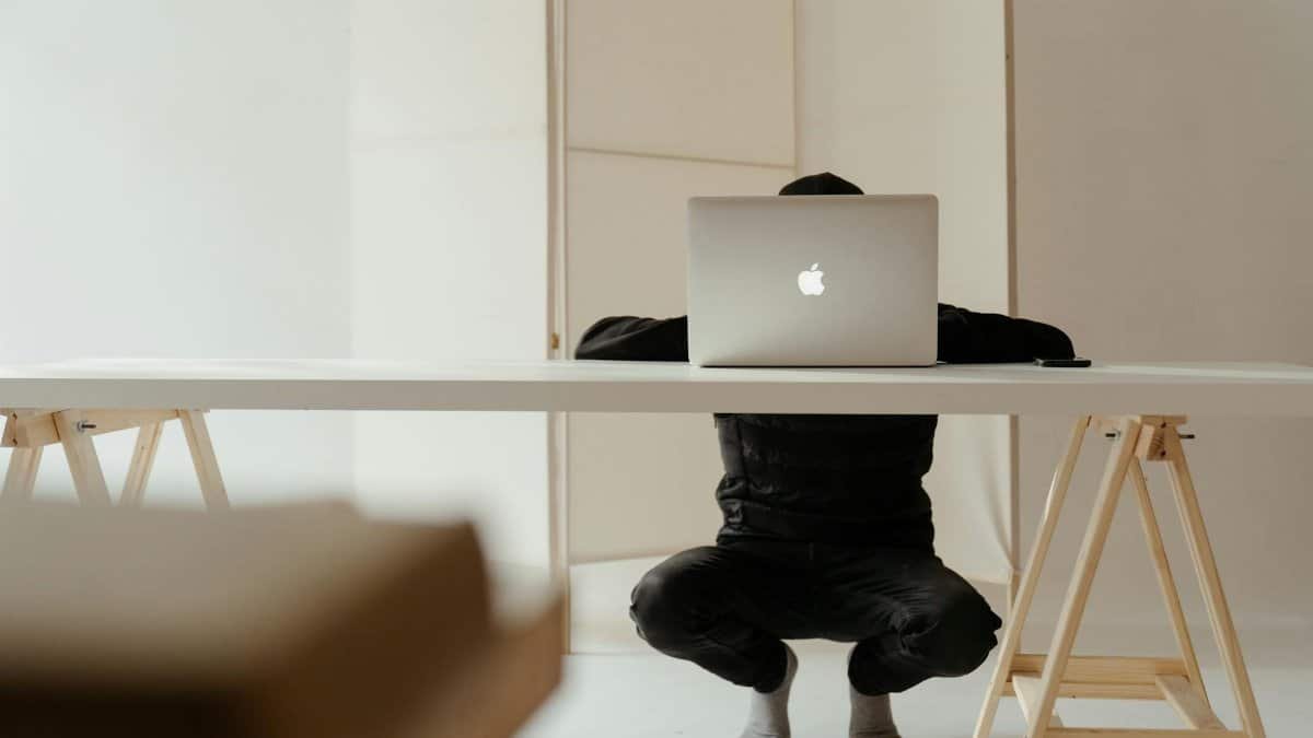 A person working in a minimalistic home office setup with a laptop on a white table.