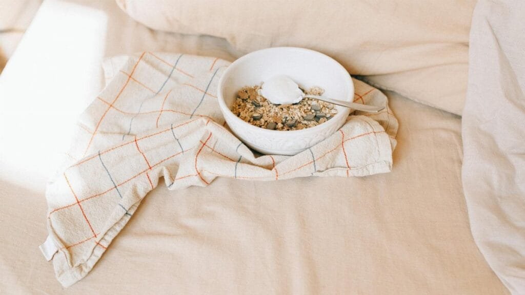A bowl of granola with yogurt on a bed, exuding a cozy morning ambiance.