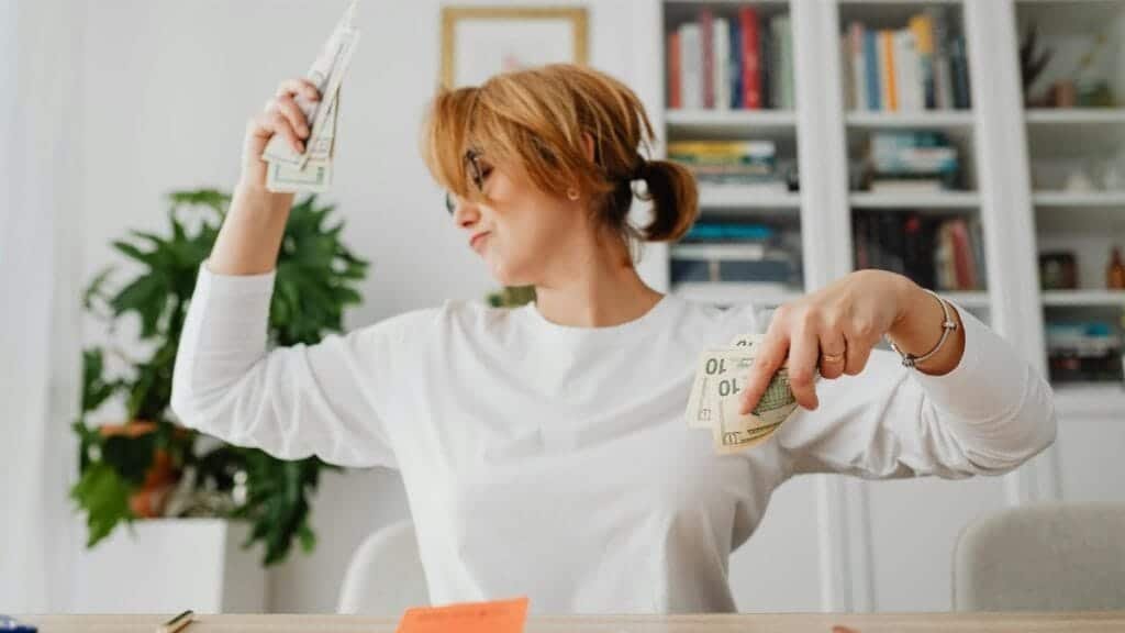 Woman in living room joyfully counting cash, expressing financial success and happiness.