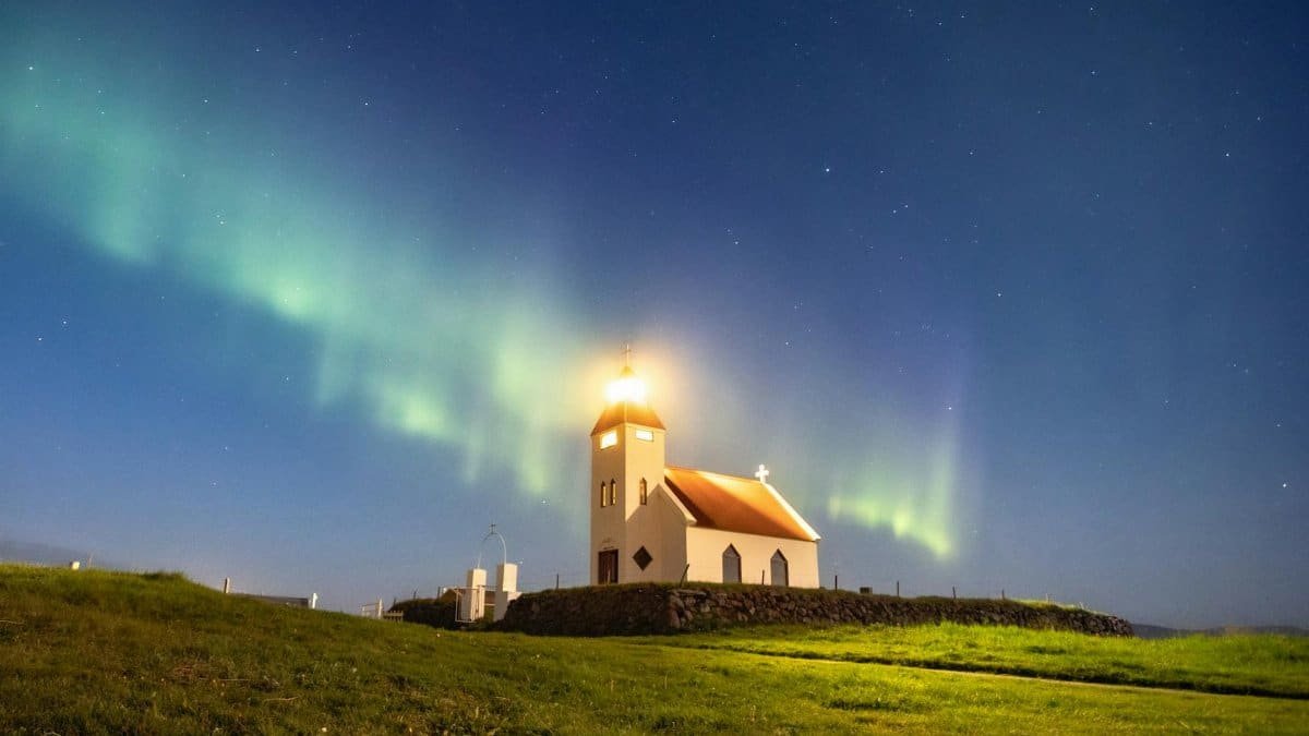 A stunning view of the Northern Lights illuminating a church in Iceland under a clear night sky.