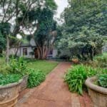 Lush green garden path with potted plants leading to a quaint cottage.