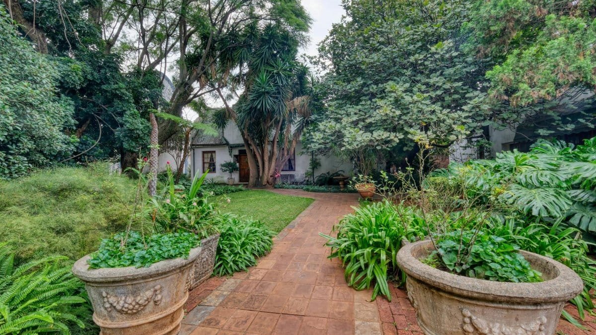 Lush green garden path with potted plants leading to a quaint cottage.