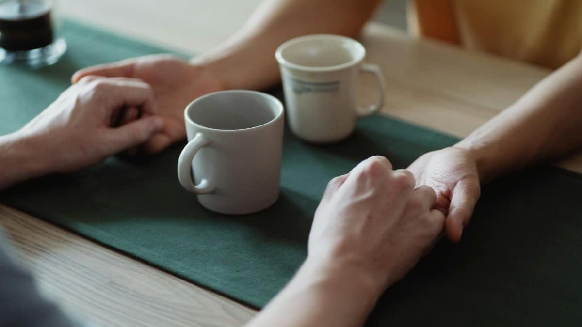 Close-up of hands holding across a table with coffee cups, conveying warmth and connection.