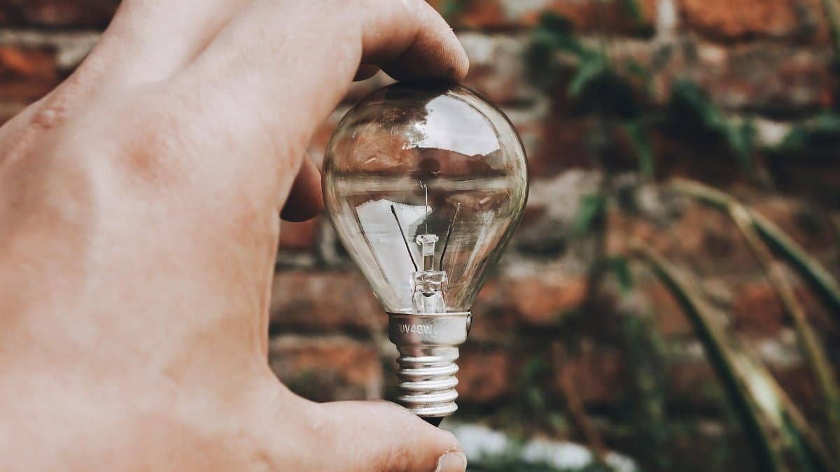 Close-up of hand holding a clear light bulb with a brick wall background, capturing innovative and eco-friendly themes.