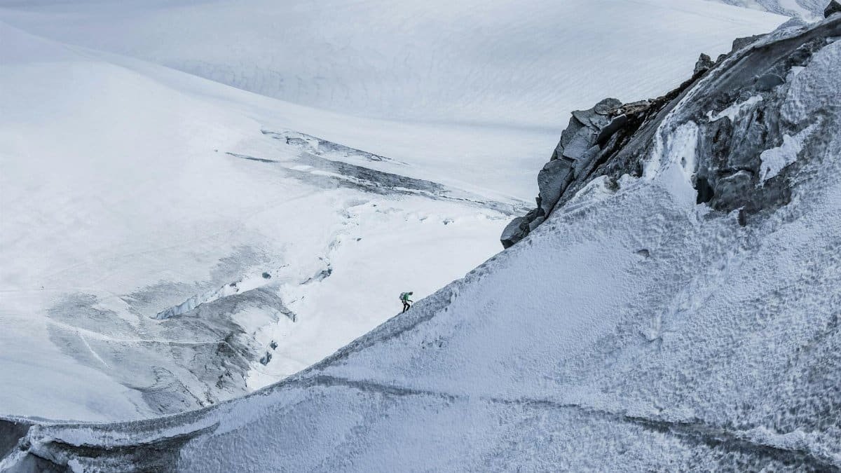 From above distant alpinist on snowy rough mountain slope against frozen spacious mountainous valley in daylight
