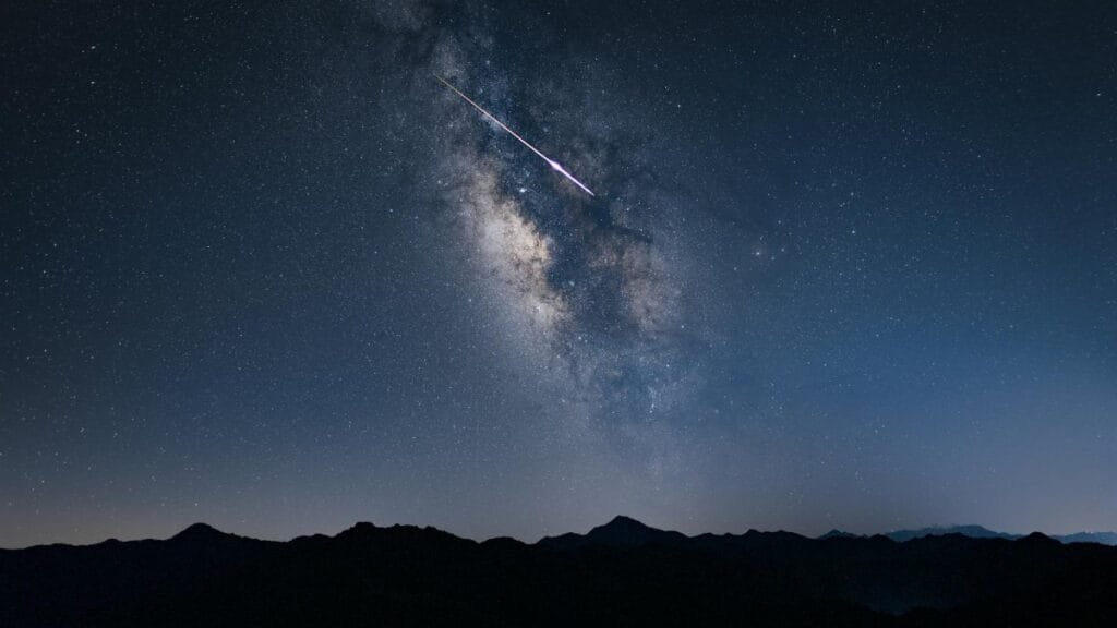 Beautiful night sky featuring the Milky Way galaxy and a shooting star over mountain silhouettes.